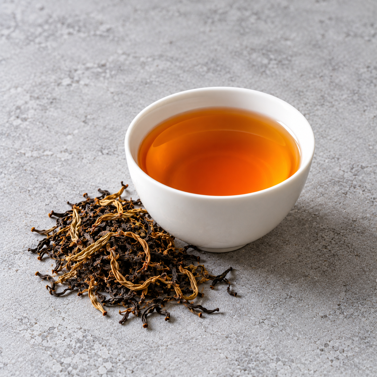 A cup of Darjeeling Second Flush, amber in colour, beside its dry whole leaf
